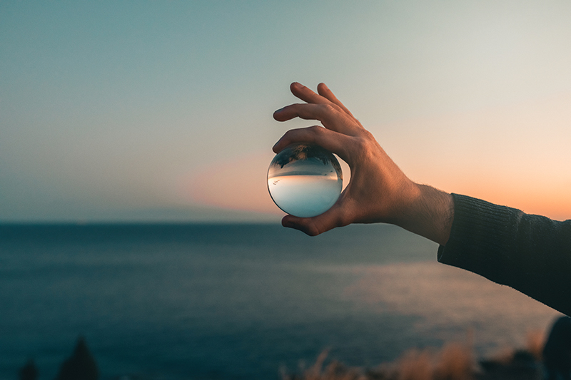 A hand holding a glass sphere above a landscape